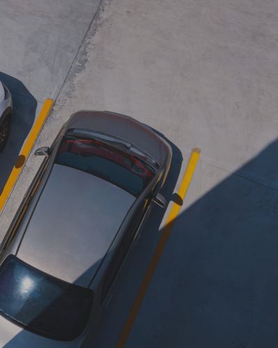 Auf einem Parkplatz steht ein silbernes Auto zwischen gelben Linien – eine typische Szene, die ein effizientes Parkraummanagement widerspiegelt. Das Auto befindet sich teilweise im Schatten, während in der Nähe der Beton und ein Teil eines anderen Fahrzeugs zu sehen sind. - Sevoria Parking