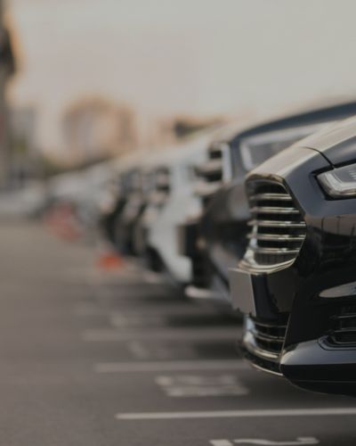 Eine Reihe geparkter Autos auf einem Parkplatz, wobei der Fokus auf der Frontpartie eines schwarzen Autos im Vordergrund liegt. Der Hintergrund ist unscharf und zeigt weitere in einer Reihe stehende Fahrzeuge – eine ideale Szene für effiziente Parkraummanagement- oder ANPR-Systeme zur Optimierung der Fahrzeugverfolgung und -organisation. - Sevoria Parking