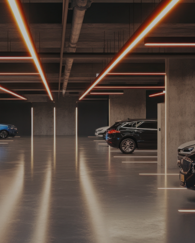 Eine moderne Tiefgarage mit eleganten Autos, die entlang der Betonsäulen geparkt sind, beleuchtet von langen, orangefarbenen LED-Deckenleuchten, deren Licht sich auf dem glänzenden Boden spiegelt – ein Paradebeispiel für effizientes Parkraummanagement, das darauf ausgelegt ist, den Parkraum für den Einzelhandel zu optimieren und den Besuchern ein nahtloses Erlebnis zu bieten. - Sevoria Parking