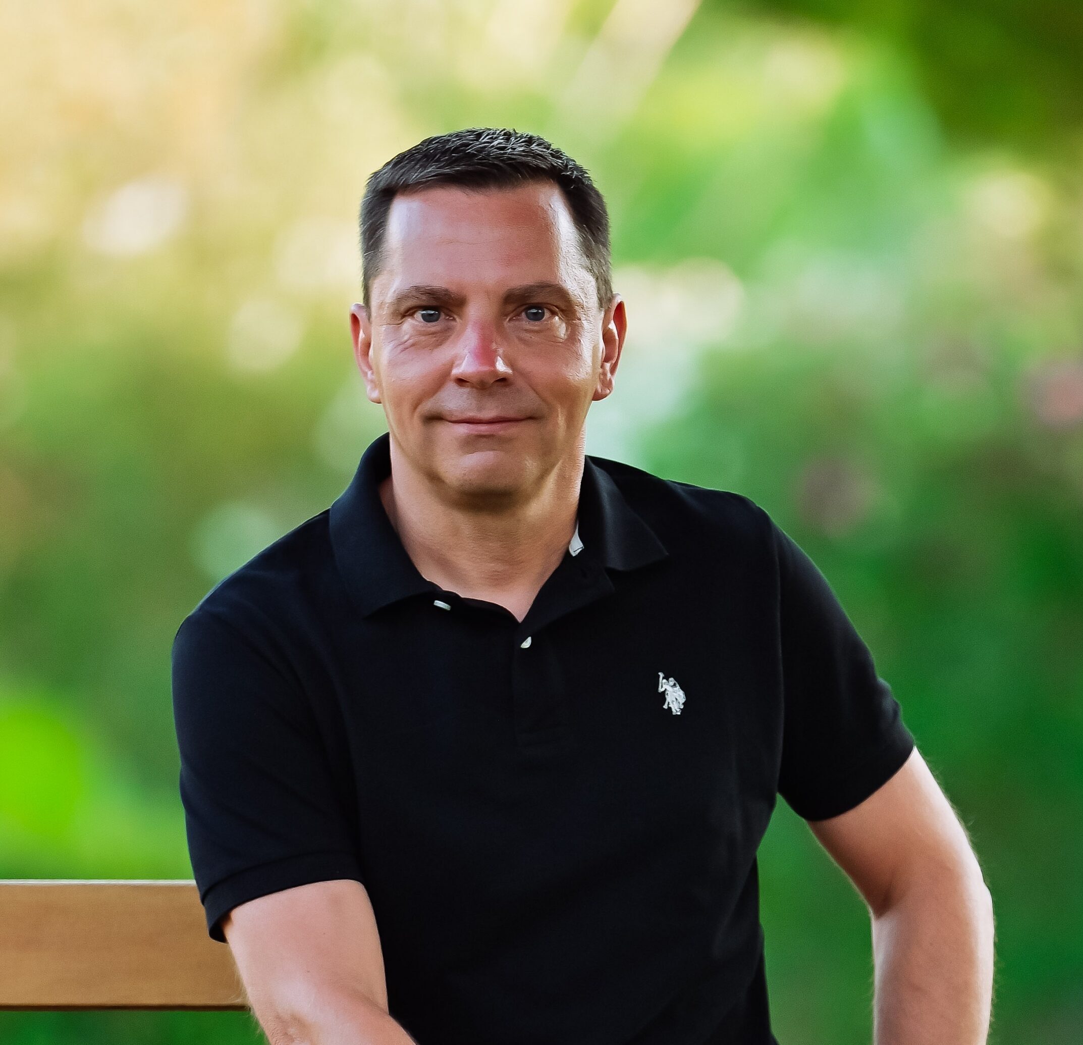 Ein Mann in einem schwarzen Poloshirt sitzt draußen auf einer Holzbank – eine Kulisse, die sich gut für eine Flächenanalyse eignet. - Sevoria Parking